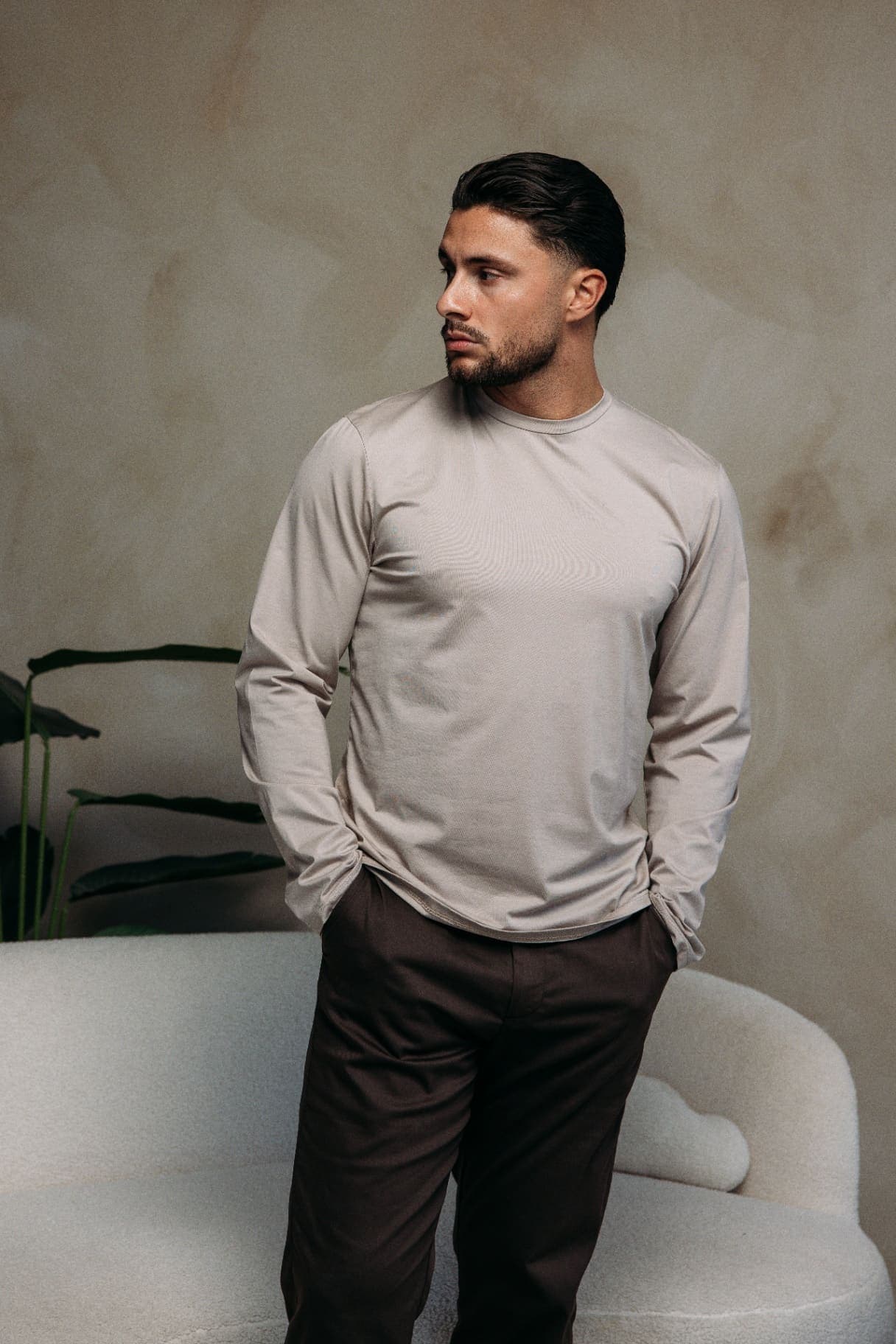 Model in een beige longsleeve en donkerbruine pantalon voor een boucle bank