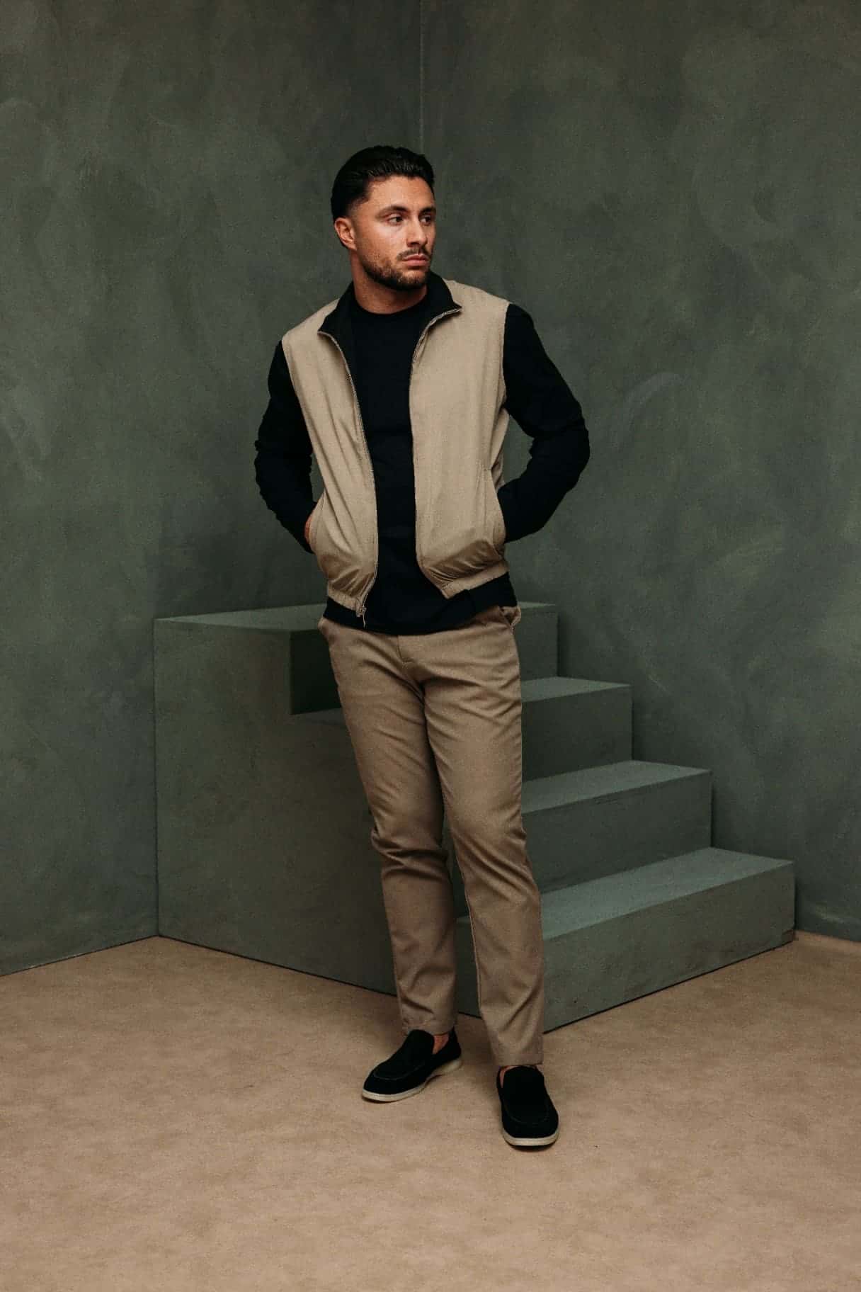 Model in a beige bodywarmer over a black longsleeve and beige trousers